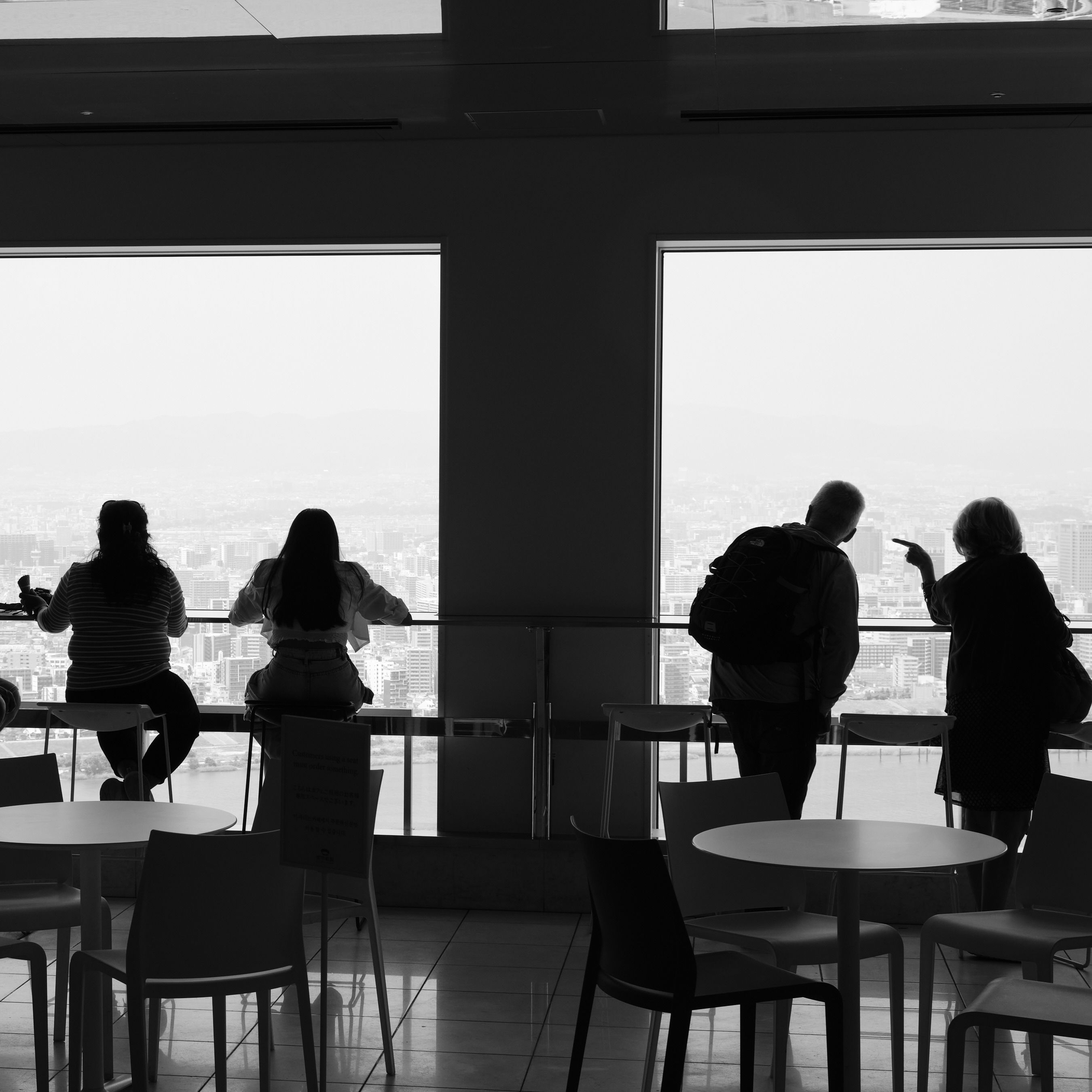 Black and white photo of people inside Umeda Sky Building in Osaka. They look out of the windows.